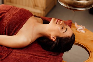 ayurvedik işlem sırasında shirodhara gemi altında yatan rahat genç kadın
