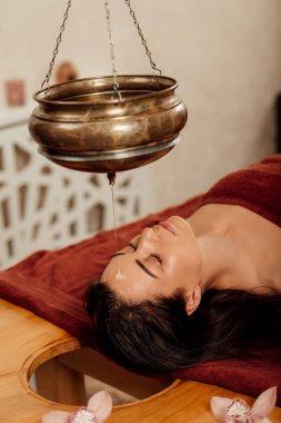 ayurvedik işlem sırasında shirodhara gemi altında yatan rahat genç kadın