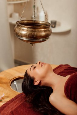 ayurvedik işlem sırasında shirodhara gemi altında yatan rahat genç kadın