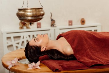 ayurvedik işlem sırasında shirodhara gemi altında yatan rahat genç kadın