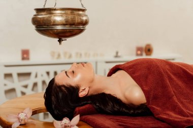 ayurvedik işlem sırasında shirodhara gemi altında yatan kadının yan görünümü