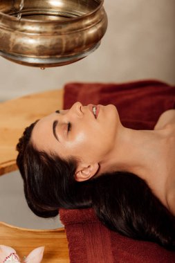 ayurvedik işlem sırasında shirodhara gemi altında yatan rahat genç kadın