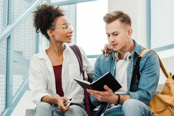 Två Multiethinc Studenter Med Anteckningsbok Sitter Trappor Universitetet — Stockfoto