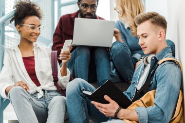 üniversitede dizüstü bilgisayar ve akıllı telefon kullanan dört gülümseyen çok ırklı öğrenci