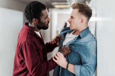 two multiethnic students fighting in corridor in college clipart