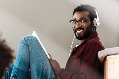 african american student in headphones using digital tablet in university clipart