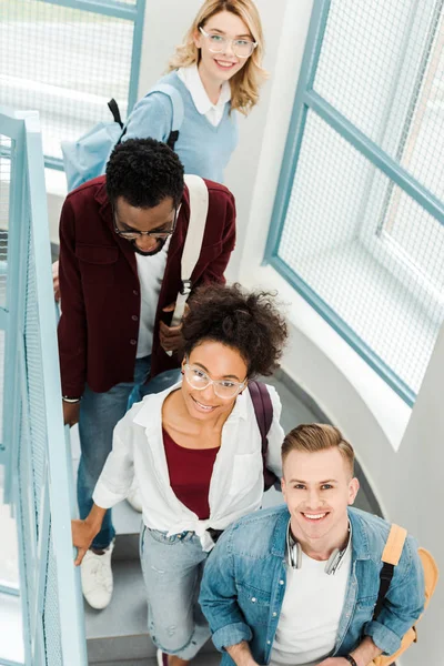 四个微笑的多民族学生背着背包在楼梯上的头顶视图 — 图库照片