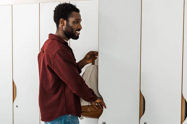 Estudiante Afroamericano Sonriente Poniendo Mochila Casillero — Foto de Stock