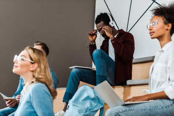 african american student with digital tablet listening music in headphones in lecture hall