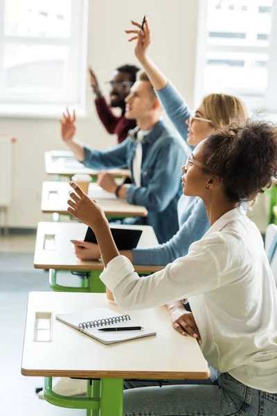 Messa Fuoco Selettiva Studenti Multietnici Seduti Alle Scrivanie Alzando Mani — Foto Stock