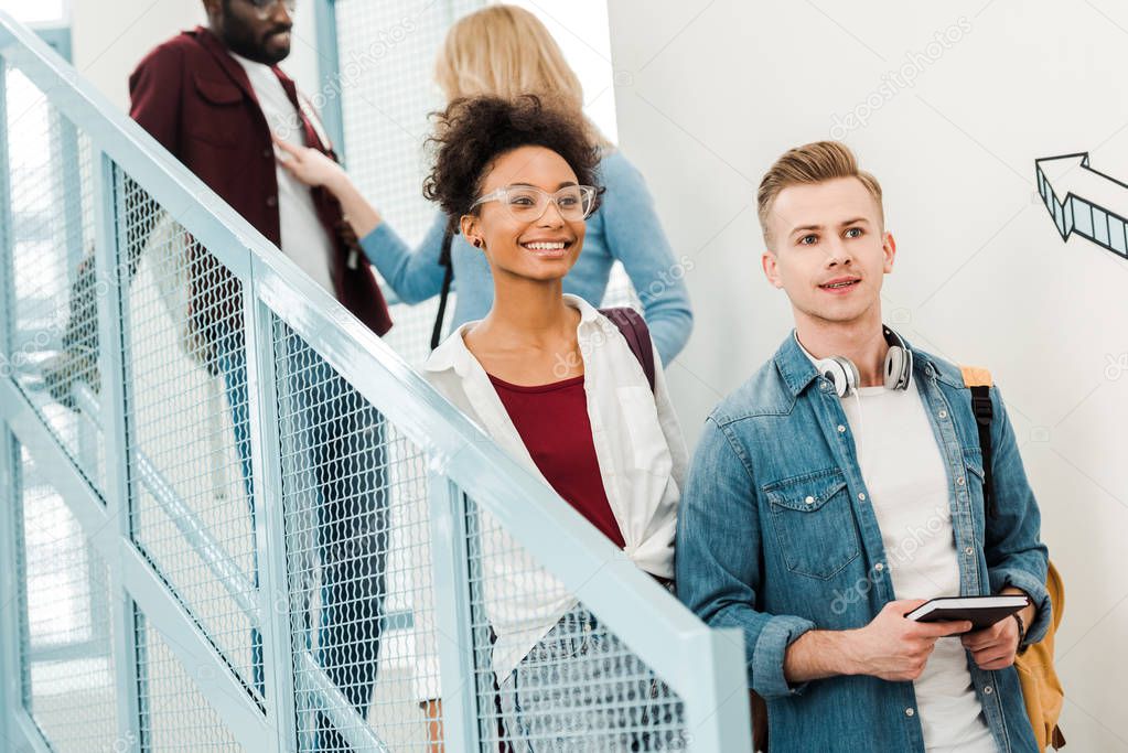 four smiling multiethnic students with backpacks on stairs