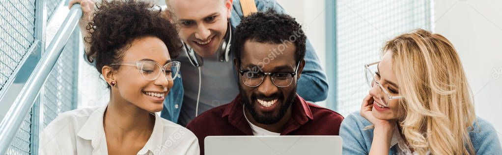 panoramic shot of smiling multicultural students with laptop in university