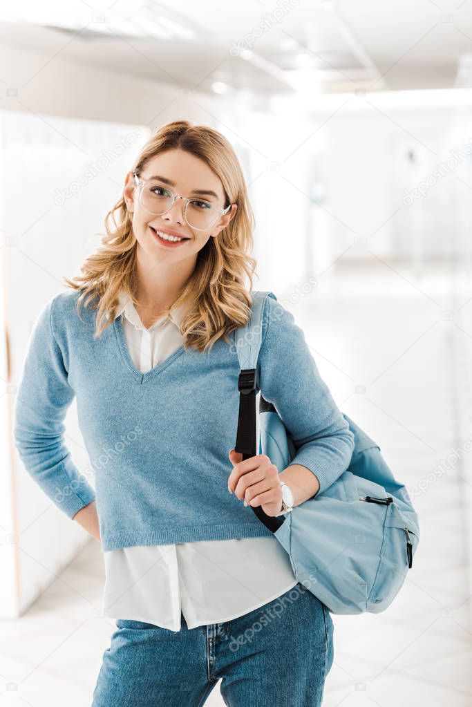 smiling student in glasses with backpack in corridor in college
