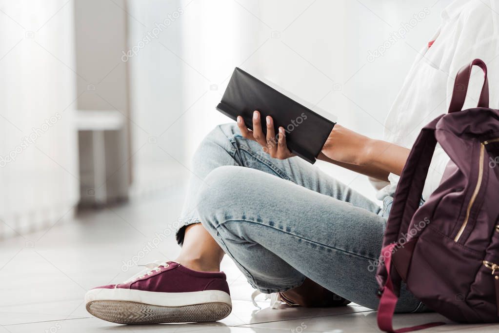 partial view of student with notebook sitting on floor