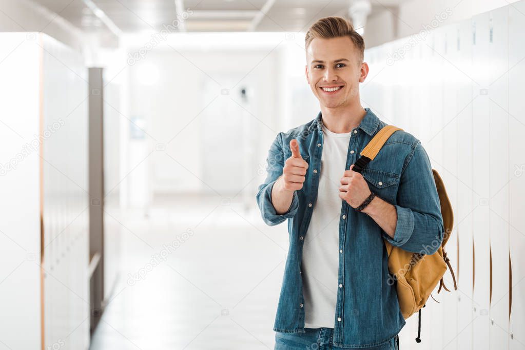 student with backpack showing thumb up in corridor in university