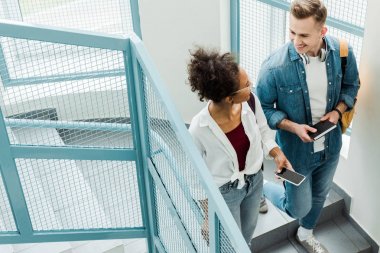 merdivenlerde duran dizüstü bilgisayar ve akıllı telefon ile iki öğrencinin havai görünümü