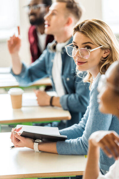 симпатичный студент в очках держит ноутбук и смотрит в камеру во время лекции
