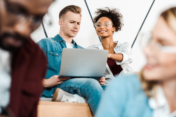 smiling multicultural students using laptop in lecture hall