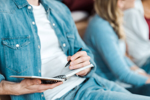 cropped view of student in denim shirt holding pen and notebook