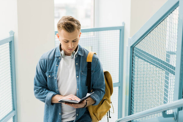 concentrated student in denim shirt and headphones with yellow backpack in university