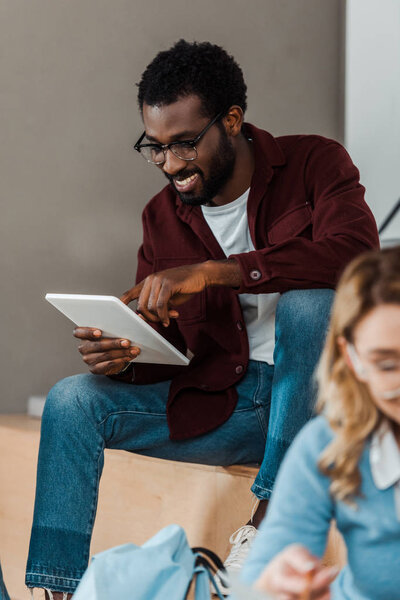 smiling african american student in glasses using digital tablet