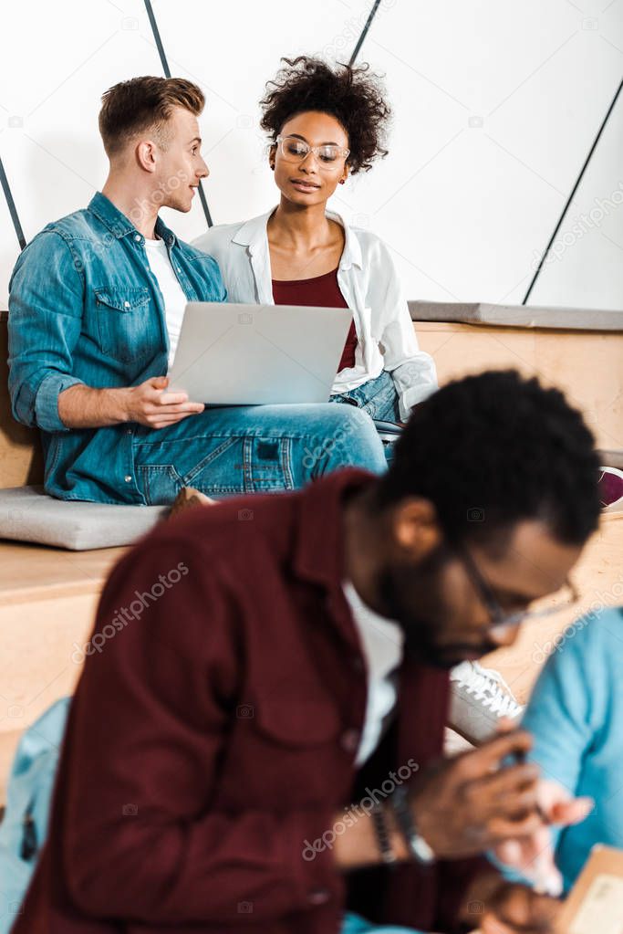 multicultural students in glasses using laptop in lecture hall