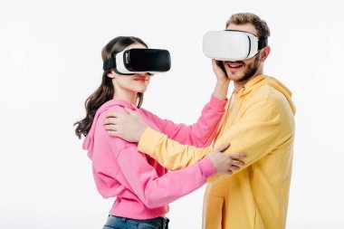 Genç adam ve kadın kucaklaşırken sanal gerçeklik kulaklıklarını beyaza takıyorlar.