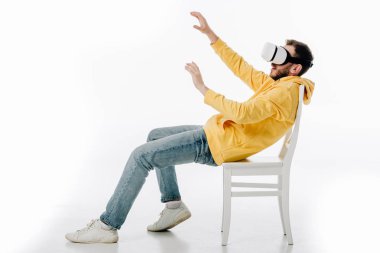 Geniş elleri olan genç adam, beyaz arka planda sanal gerçeklik kulaklığıyla sandalyede oturuyor.