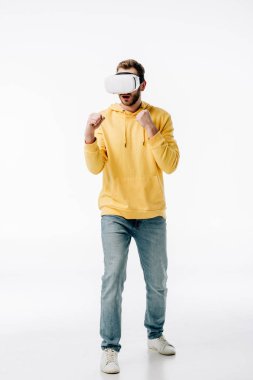 Beyaz arka planda sanal gerçeklik kulaklığı kullanırken mavi kot ve sarı kapüşonlu genç adam boksu taklit ediyor.