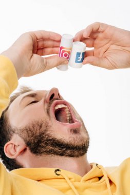 Genç sakallı adam Facebook ve instagram logolarının bulunduğu konteynırdan hap yutuyormuş gibi yapıyor.