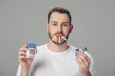Ağzında sigarası olan, Instagram logosu olan ve gri renkli kameraya bakan genç adam.