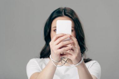 Gri renkte izole edilmiş akıllı telefon kullanan ellerinde USB kablosu olan genç bir kadın.
