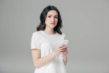 gri izole akıllı telefon kullanarak elleri etrafında beyaz t-shirt ve usb kablosu çekici genç kadın