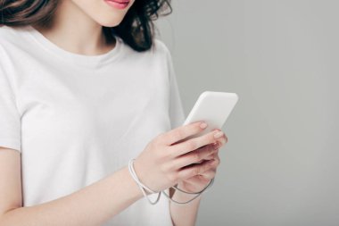 gri izole akıllı telefon kullanarak elleri etrafında beyaz t-shirt ve usb kablosu genç kadının kırpılmış görünümü