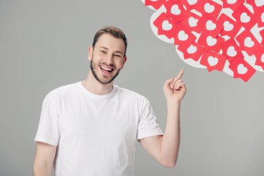 beyaz t-shirt neşeli genç adam kırmızı kağıt kesilmiş kartları ile işaret kalpleri sembolleri gri izole
