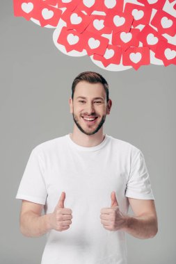 beyaz t-shirt yakışıklı genç adam gri izole kalpleri sembolleri ile kırmızı kağıt kesme kartları yakınında başparmak gösteren
