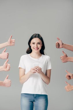 cropped view of men and women showing thumbs up near happy girl with smartphone isolated on grey clipart