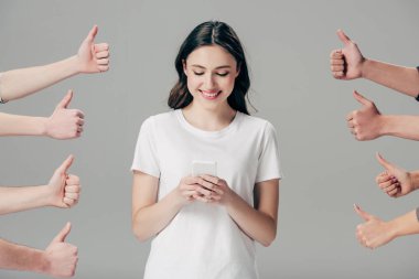 partial view of men and women showing thumbs up near happy girl using smartphone isolated on grey clipart