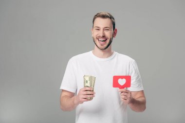 beyaz t-shirt tutan mutlu yakışıklı adam dolar banknotlar ve kalp sembolü gri izole kırmızı kağıt kesme kartı
