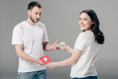 gri arka plan üzerinde kalp sembolü ile kırmızı kağıt kesme kartı ile çekici kadına dolar banknotlar veren yakışıklı genç adam