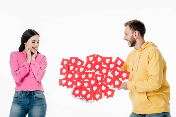 handsome young man gifting red paper cut cards with hearts symbols to smiling girl isolated on white