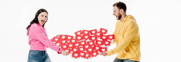 panoramic shot of young couple quarreling while holding red paper cut cards with hearts symbols isolated on white