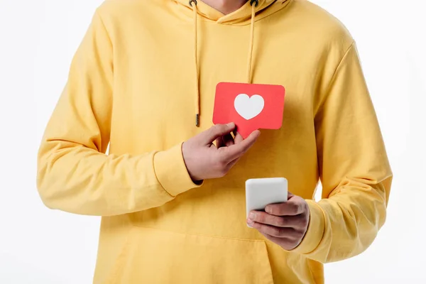 部分视图的人在黄色连帽衫使用智能手机和持有红色纸切卡与心脏符号隔离在白色 — 图库照片