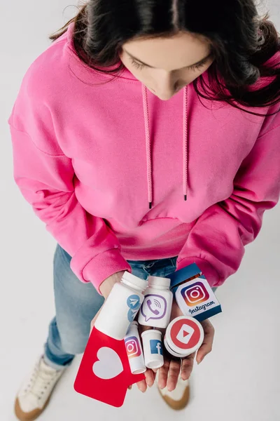 ソーシャルメディアのロゴと灰色の背景にハートのシンボルを持つ赤い紙カットカードとコンテナを保持している女の子のオーバーヘッドビュー — ストック写真