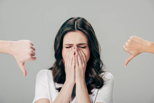 cropped view of man and woman showing thumbs down near upset girl holding hands on face isolated on grey