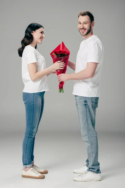 英俊的年轻人赠送红玫瑰花束漂亮的女朋友在灰色背景 — 图库照片