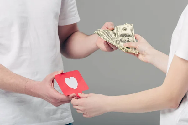 部分观点男子赠送美元钞票的女人拿着红色纸切卡与心脏符号隔离在灰色 — 图库照片
