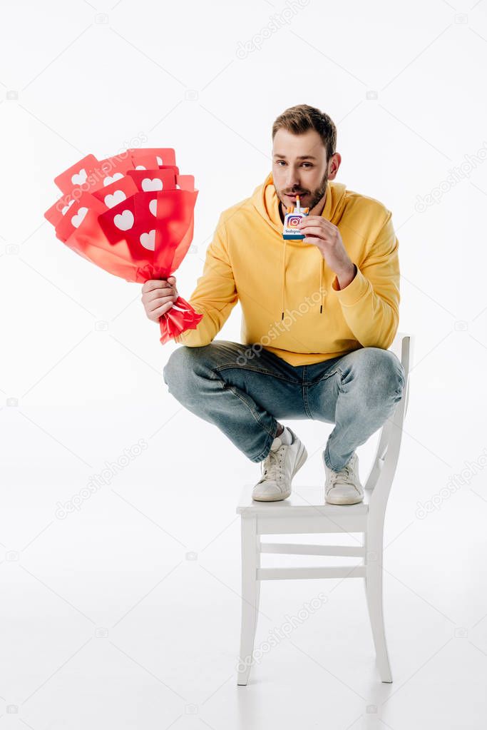 Smiling man with bouquet of red paper cut cards with hearts symbols holding cigarette pack with instagram logo on white background