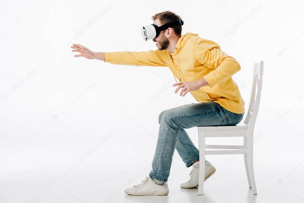 young man in virtual reality headset sitting on chair with outstretched hand on white background