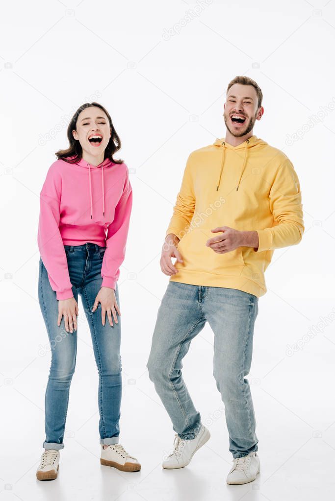 cheerful young man and woman in blue jeans and hoodies laughing while looking at camera on white background 